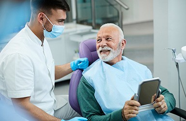 Senior patient looking at dentist while holding small mirror