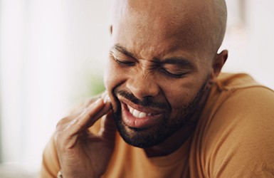 Man squinting face holding hand to cheek in pain