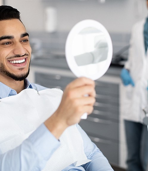 Man smiling at reflection in handheld mirror