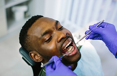 Man undergoing dental exam by dentist in blue gloves