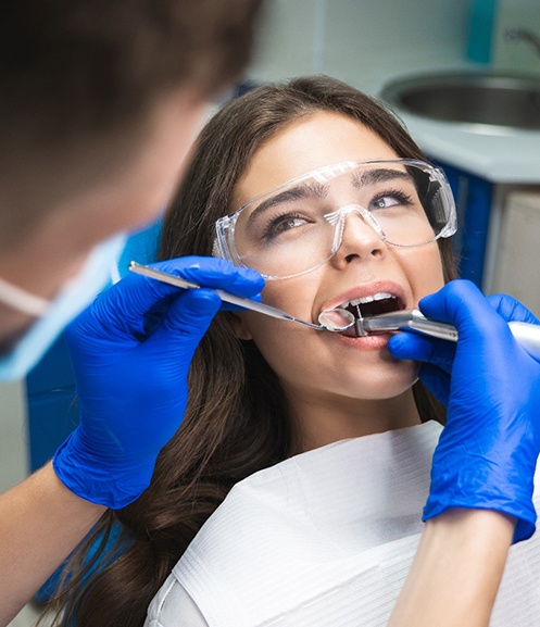 Woman in clear goggles looking at dentist performing root canal on her tooth