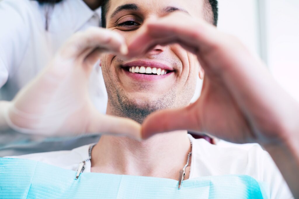 Man and his dentist forming finger heart around his smile