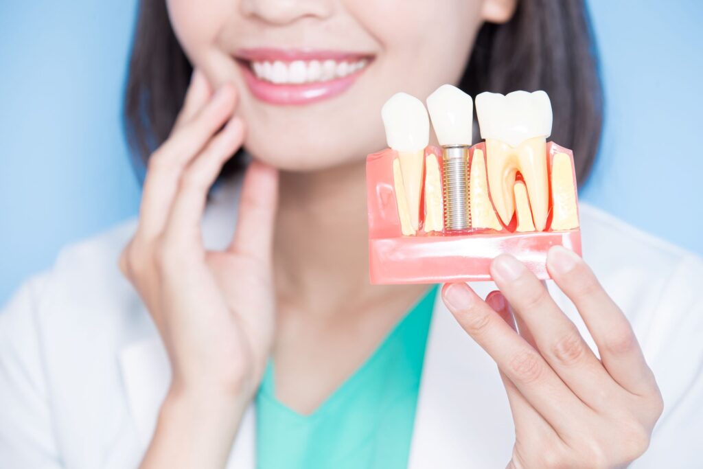 Dentist touching cheek with one hand holding sample implant in the other